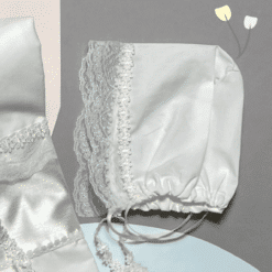 Λευκό καπελάκι με δαντελένιο τελείωμα και κορδέλα, τοποθετημένο πάνω σε παστέλ φόντο μαζί με λευκά υφάσματα.