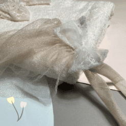 Κοντινό λήψης εκρού και λευκού τούλιου με φιόγκο και δαντέλα πάνω σε λευκή πετσέτα, με παστέλ γραφικά λουλουδάκια στη γωνία.